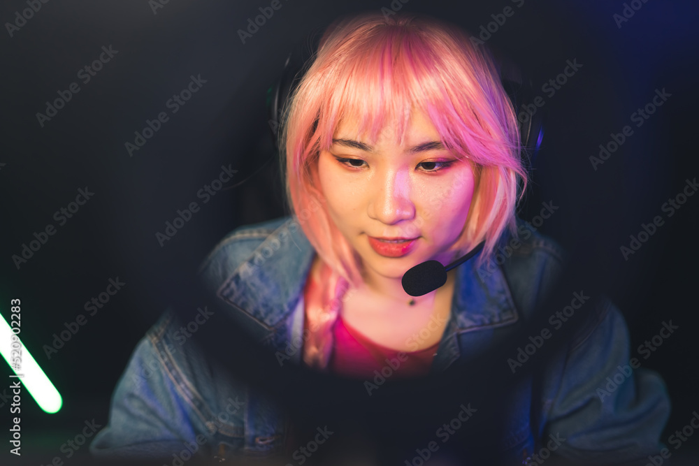 Fototapeta premium Teenage asian girl with pink braided hair wearing headset focused on playing competitive game. High quality photo