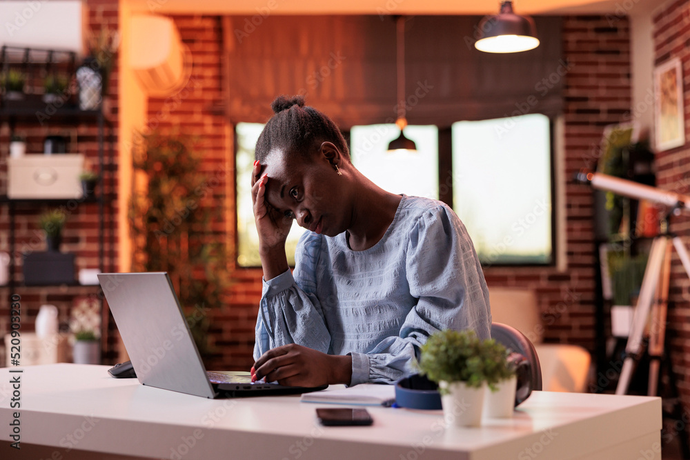 Overworked young female freelancer working on laptop in modern home office, burnout and workload concept. Stressed and exhausted african american businesswoman having headache