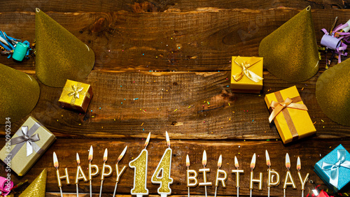 golden letters of the candle with the number happy birthday, the background of the gift boxes with candles happy birthday on the background of brown boards. Copy spacePostcard Happy birthday 14. photo