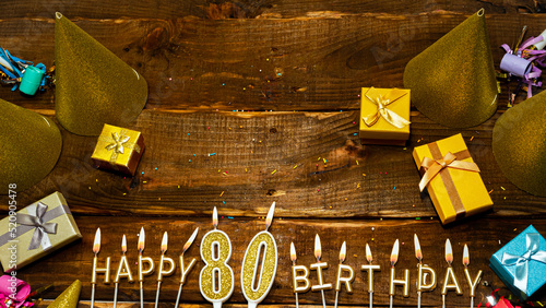 golden letters of the candle with the number happy birthday, the background of the gift boxes with candles happy birthday on the background of brown boards. Copy spacePostcard Happy birthday 80 photo