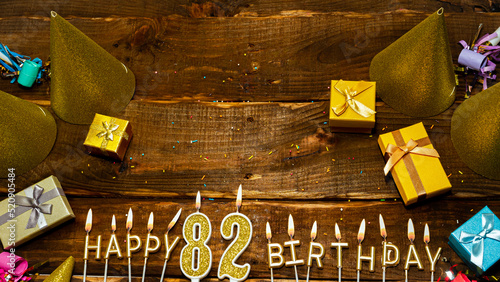 golden letters of the candle with the number happy birthday, the background of the gift boxes with candles happy birthday on the background of brown boards. Copy spacePostcard Happy birthday 82. photo