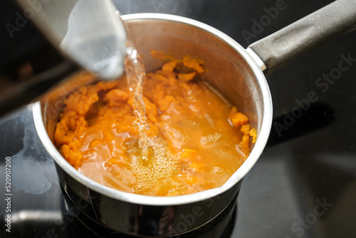 Pureed carrots are poured with boiling water in a steel pot, cooking a healthy digestible vegetable soup, invented by Professor Moro against diarrhea, selected focus, narrow depth of field