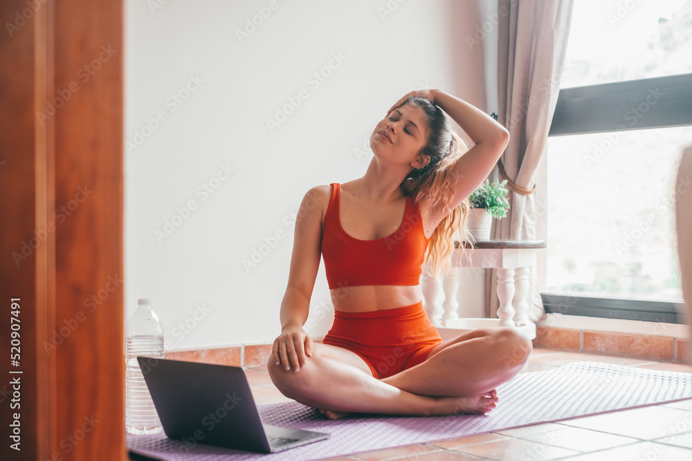 Obraz premium Portrait of blonde beautiful woman doing yoga and relaxing her mind and her body at home on the floor. One active and heathy girl taking care of health training. Following a video tutorial on laptop 