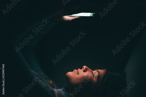 One beautiful young woman holding and using phone at home at late night on the sofa. Female teenager chatting with friends surfing the net online. Tired girl using phone with eyes closed in bedroom.