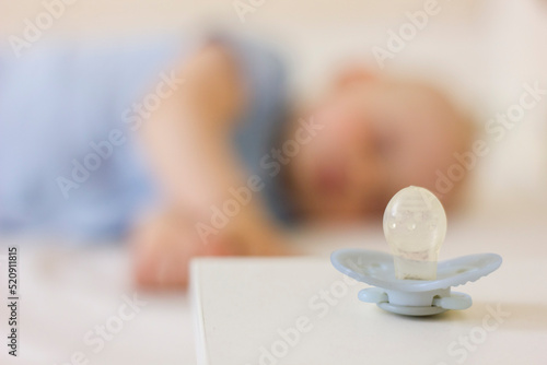 Little baby boy is peacefully sleeping and a pacifier dummy liying on table near bed.