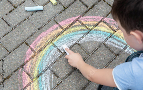 Portrait of a child drawing a rainbow on the street with colored chalk. Selective focus. Kid. A child is playing outside