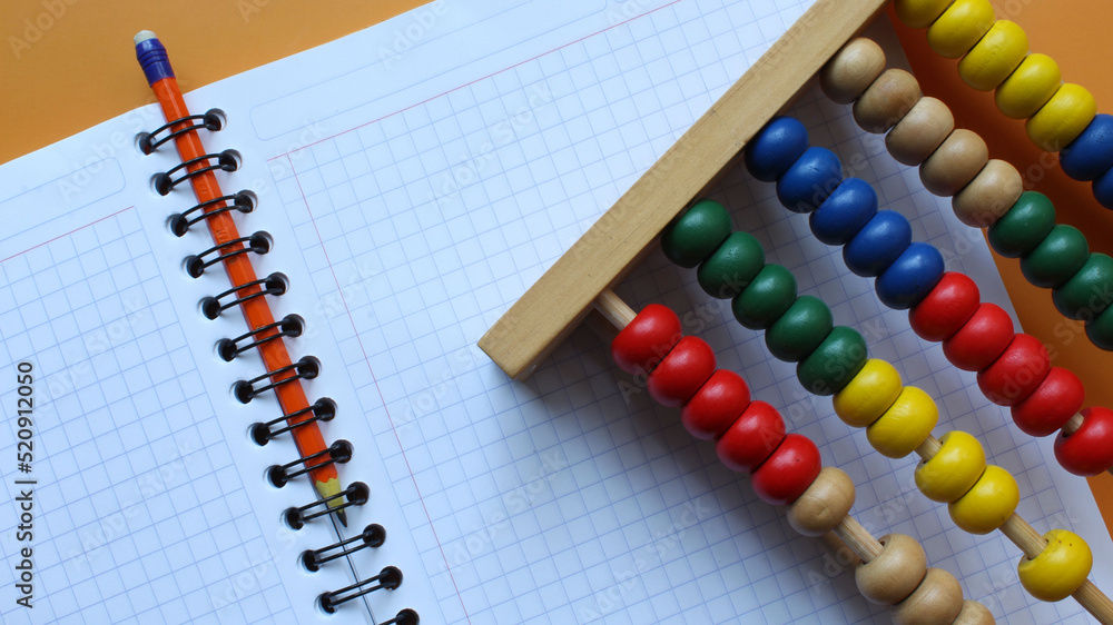 Cuaderno de cuadros con lápiz naranja y Abaco de madera con cuentas de colores. Cuaderno de cuadros con lápiz naranja y Abaco de madera con cuentas de colores.