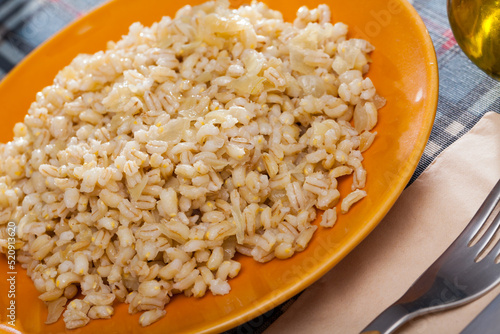 Boiled pearl barley served on yellow ceramic dish on checkered fabric surface.. photo