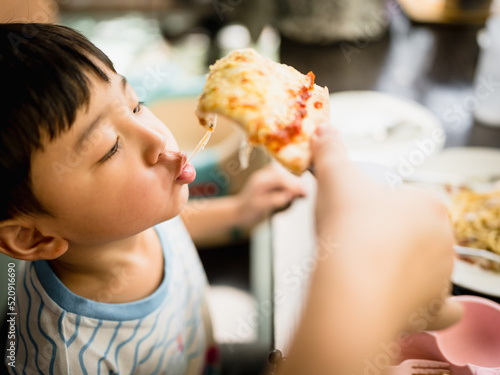 Asian boy eating pizza deliciously by pulling out the pizza by mouth. 