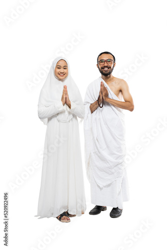 Husband and wife wearing white hajj ihram clothes with greeting gesture standing on isolated background
