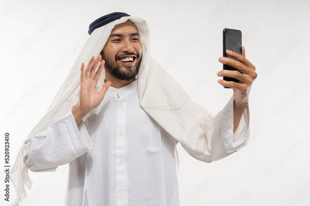 excited young man in a turban using a mobile phone happily looking at the screen waving to partner online excited young man in a turban using a mobile phone happily looking at the screen waving to partner online