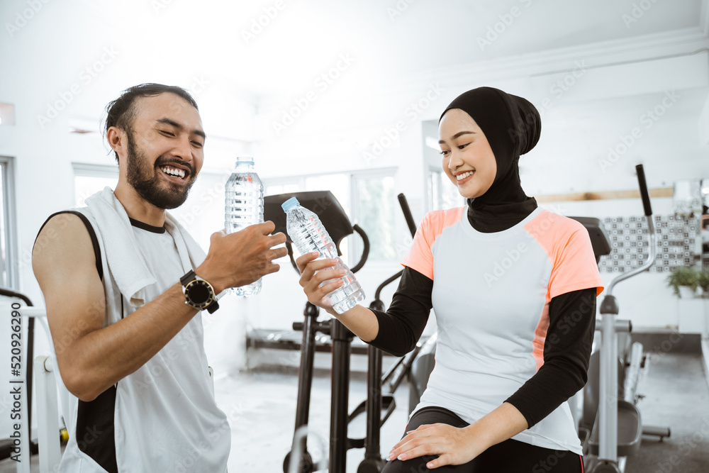 beautiful muslim couple having fun at the gym while enjoying a bottle of water together beautiful muslim couple having fun at the gym while enjoying a bottle of water together