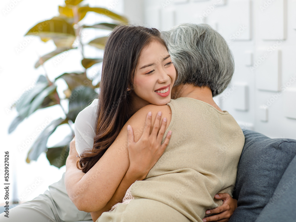 Asian cheerful young beautiful daughter sitting smiling hugging embracing showing affection love comforting bonding with old senior grey hair pensioner mother on cozy sofa in living room at home Asian cheerful young beautiful daughter sitting smiling hugging embracing showing affection love comforting bonding with old senior grey hair pensioner mother on cozy sofa in living room at home