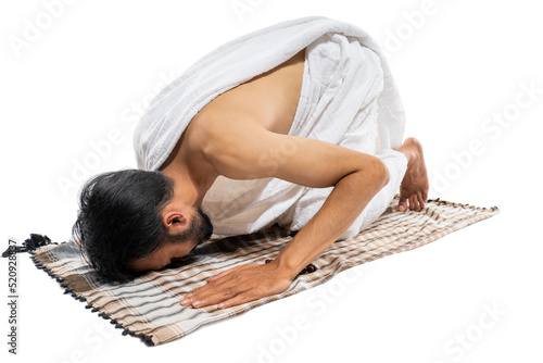 Man wearing ihram clothes praying with prayer rug while prostration on isolated background photo