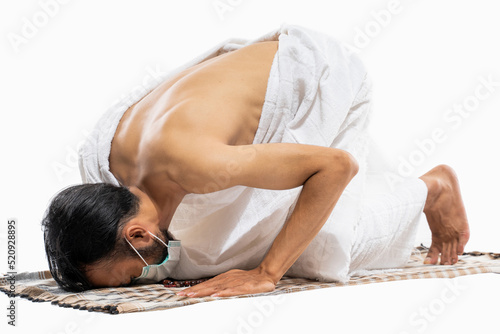 Canvas Print Man in mask wearing ihram clothes praying with prayer rug while prostration on i