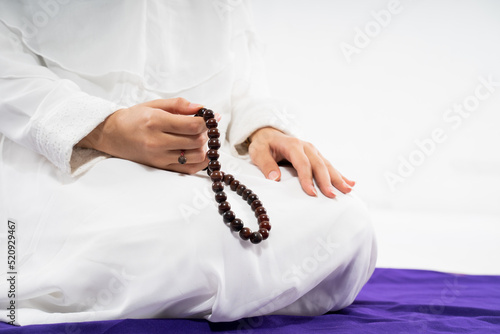 Woman's hand wearing ihram praying with prayer rug and prayer beads on isolated background