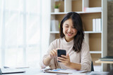 Beautiful Asian businesswoman using smartphone to view social media applications, respond to customer chats, make transactions through an application in the office.