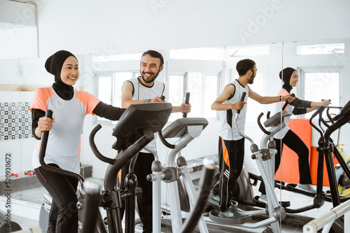 Fototapeta Naklejka Na Ścianę i Meble -  muslim women at the gym doing cardio exercises on static elliptical cycle machine