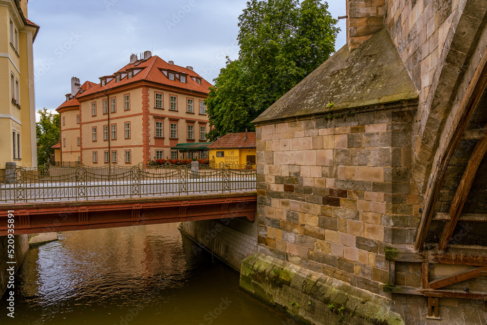 A small bridge across a river in Prague between buildings.