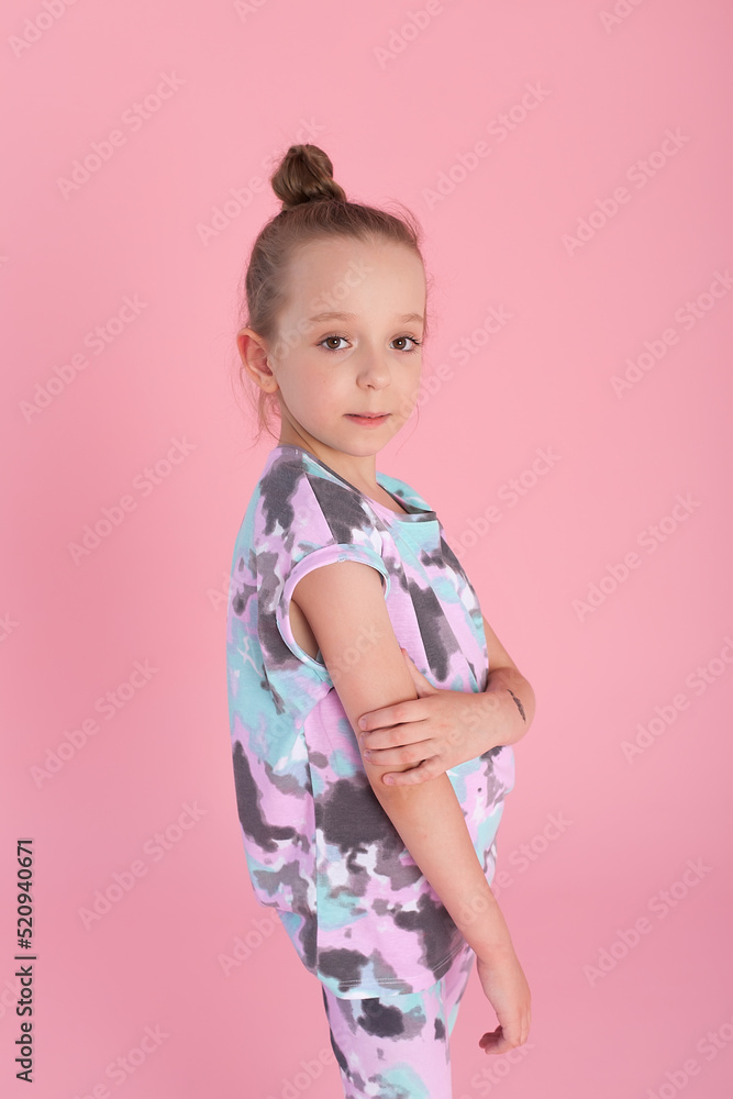 An expressive charming little girl in a bright suit stands on a pink background in the studio An expressive charming little girl in a bright suit stands on a pink background in the studio