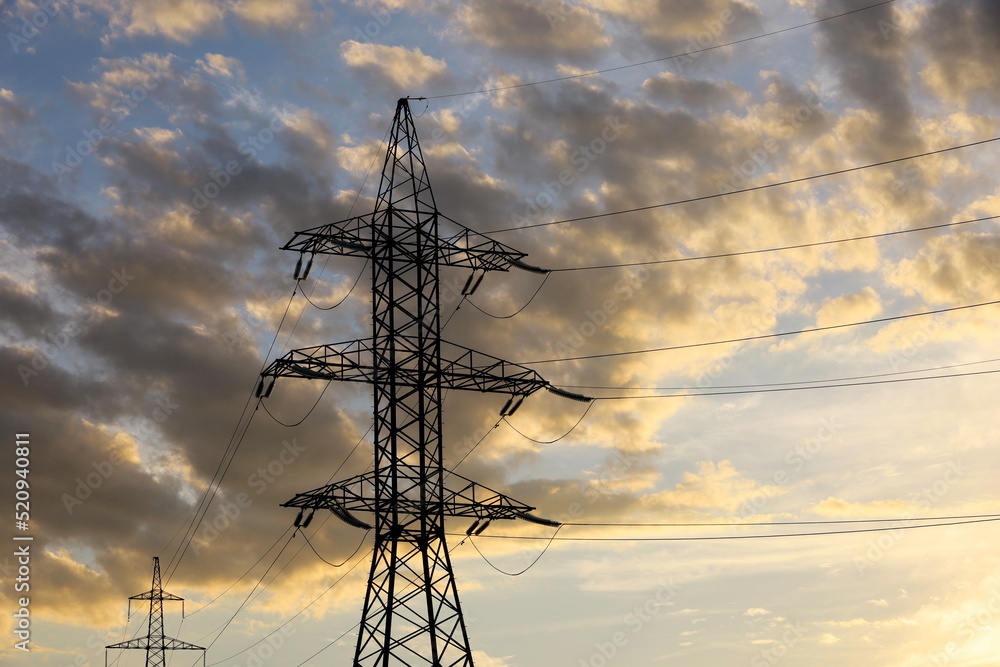 Silhouettes of high voltage towers with electrical wires on background of sunset sky and clouds. Electricity transmission lines, power supply concept
