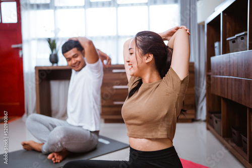 portrait of young asian couple workout together at home stretching their body