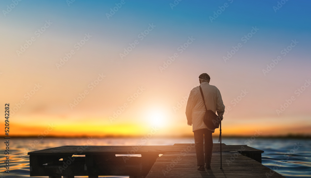 Naklejka premium old man standing alone on the pier at sunset.