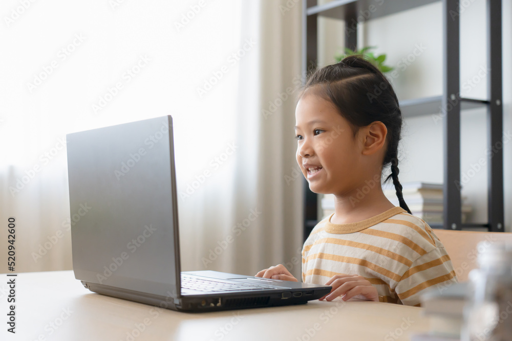 Asian school girl studying online class on laptop. Happy kid enjoy learning from home using laptop in a living room. Asian school girl studying online class on laptop. Happy kid enjoy learning from home using laptop in a living room.