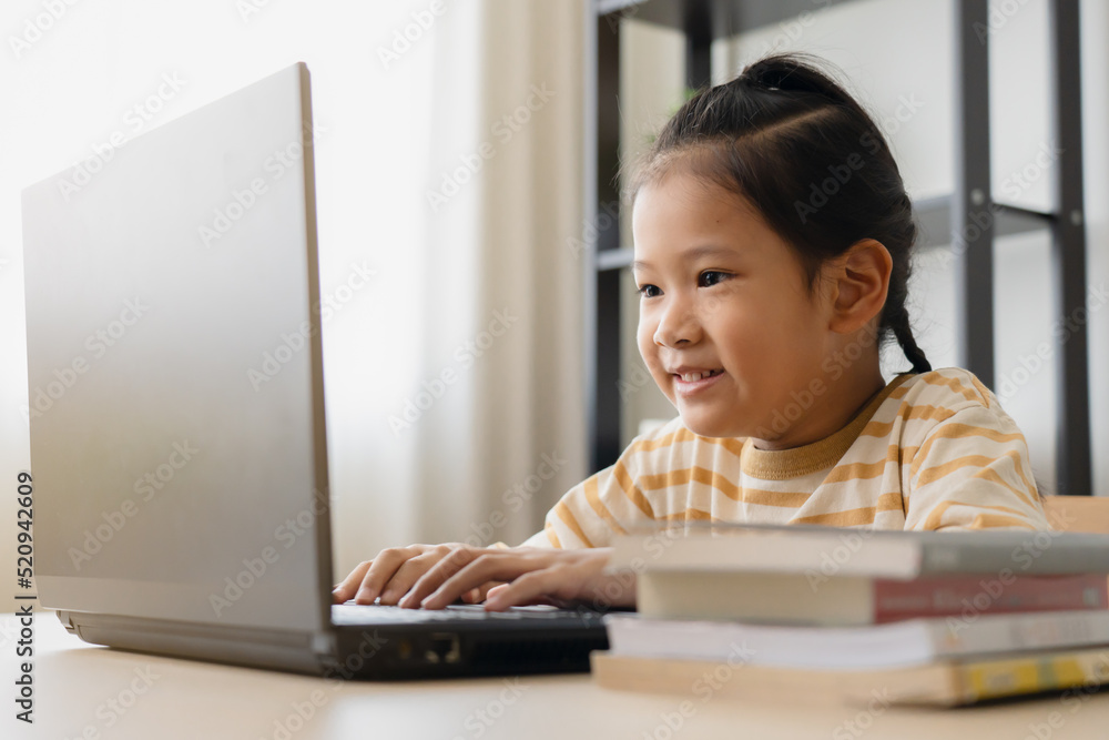 Asian school girl studying online class on laptop. Happy kid enjoy learning from home using laptop in a living room.