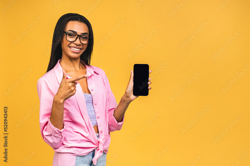 Portrait of a smiling young african american black woman holding blank screen mobile phone isolated over yellow background. Portrait of a smiling young african american black woman holding blank screen mobile phone isolated over yellow background.