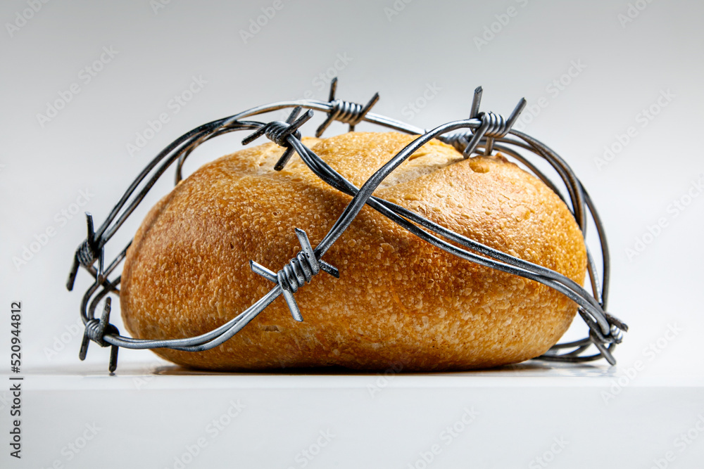 A loaf of round wheat bread wrapped with barbed wire. The concept of food crisis, food shortage