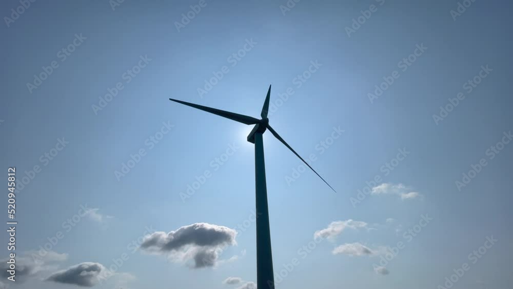 Wide shot of a wind turbine silhouetted against a bright blue sky, sun located behind the turbine. Wide shot of a wind turbine silhouetted against a bright blue sky, sun located behind the turbine.