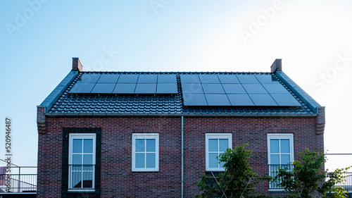 Newly build houses with solar panels attached on the roof against a sunny sky Close up of a new building with black solar panels. Zonnepanelen, Zonne energie, Translation: Solar panel, , Sun Energy.  photo