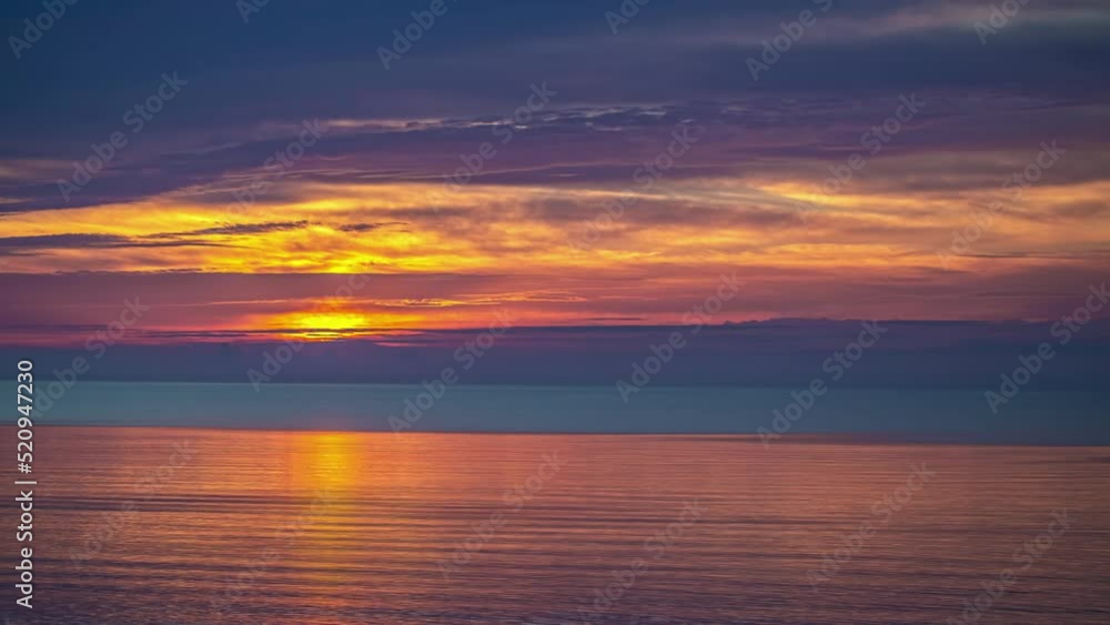 A colorful golden sunrise reflecting off the surface of the ocean on a dazzling morning - time lapse A colorful golden sunrise reflecting off the surface of the ocean on a dazzling morning - time lapse