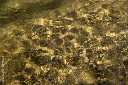 Water mountain river texture. Full frame. Fashionable light beige iridescent color of pure water. Iridescent sun and stones. Abstract natural background. Layout for wallpapers, postcards, banners.