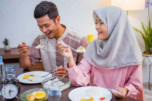 muslim couple wake up early to have sahur or suhur breakfast for fasting. clock at foreground showing the time photo