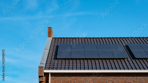 Newly build houses with solar panels attached on the roof against a sunny sky Close up of a new building with black solar panels. Zonnepanelen, Zonne energie, Translation: Solar panel, , Sun Energy.  photo