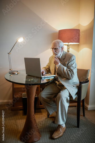 Senior man sitting at the laptop and looking busy photo