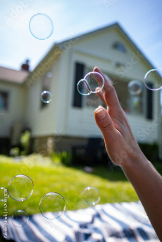 dreamy image of child's hand reaching towards blowing bubbles in suburban yard at picnic