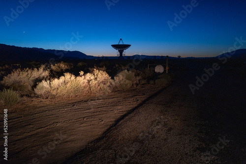 Eerie view of radio observatory under night sky with headlights on dry brush plants photo