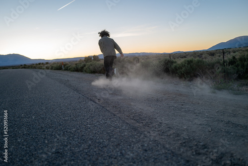 Wide shot of person with shaggy hair kicking up dust on dirt road as they run around in the middle of nowhere photo