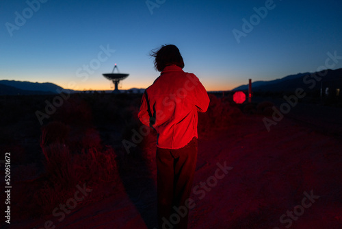 Curious stargazer, alien, and astronomy buff in moody red light explores radio observatory at night