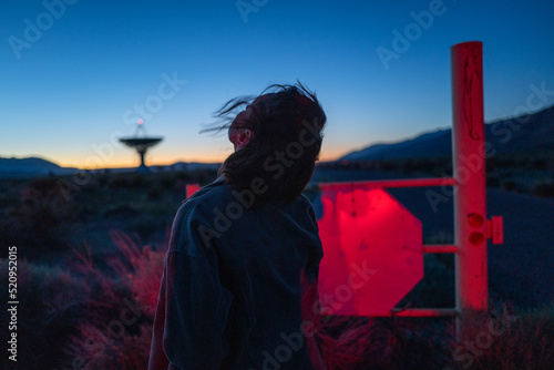 Curious stargazer and astronomy buff ponders alien life in moody red light near radio observatory under dark sky photo