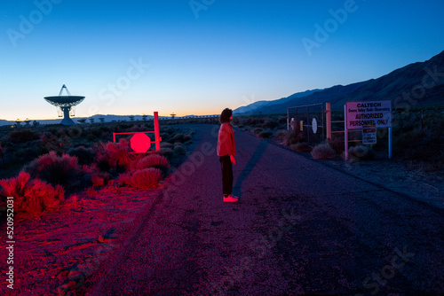Curious stargazer and astronomy buff ponders alien life in film noir red light near radio observatory under dark sky photo