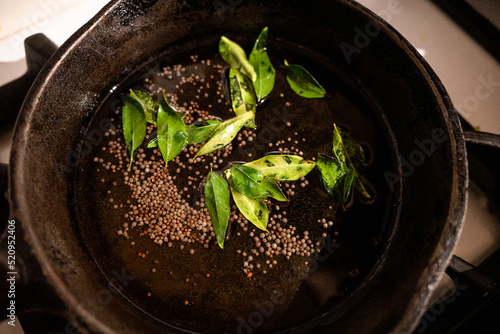 mustard seeds and green leaves in a cast iron skillet with oil photo