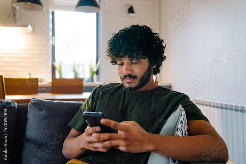 Obraz na płótnie Young indian handsome calm man sitting on sofa with phone