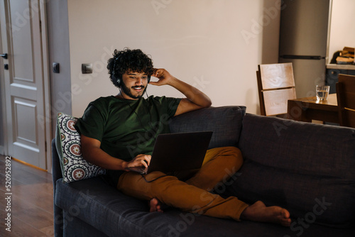 Young indian curly handsome man in headphones with laptop © Drobot Dean