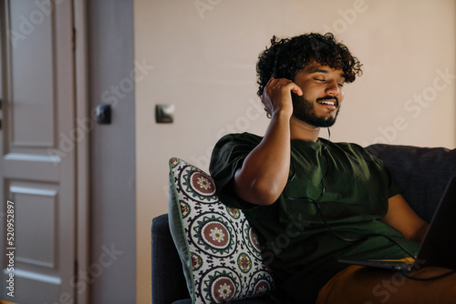 Young indian curly handsome man in headphones with laptop