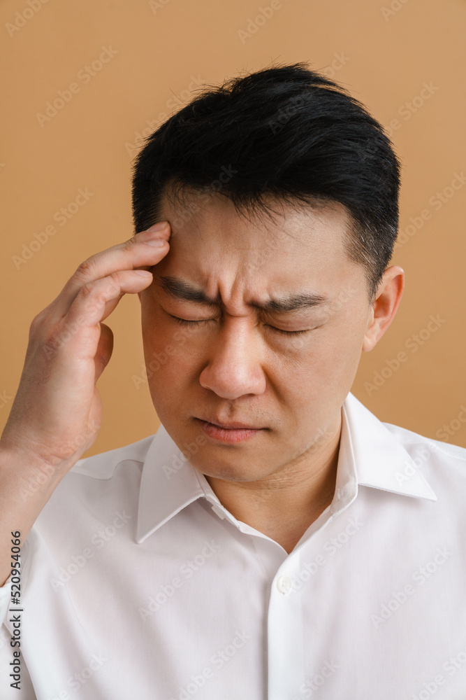 Brunette adult asian man wearing shirt rubbing his temple Brunette adult asian man wearing shirt rubbing his temple