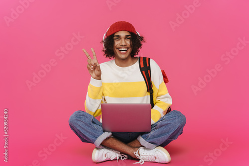 Young caribbean man in headphones gesturing and using laptop